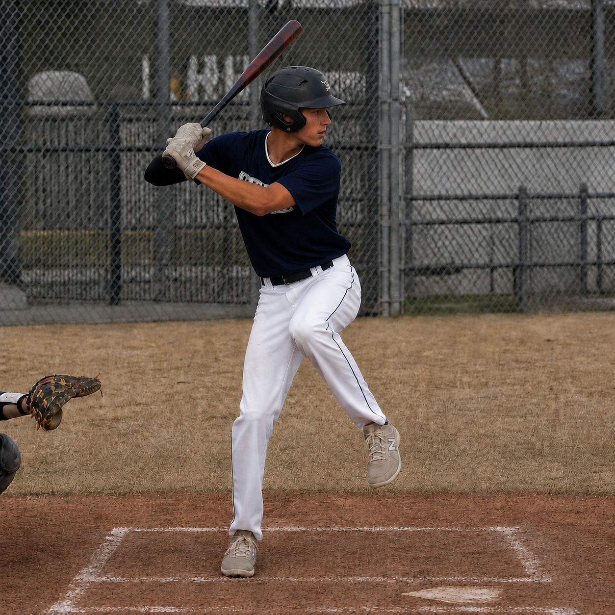 Teenage hitter mid-load — hands drawn back, back hip coiled inward, front foot lifting